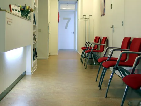 Wachtruimte met rode stoelen en de balie van de praktijk aan de Velperweg